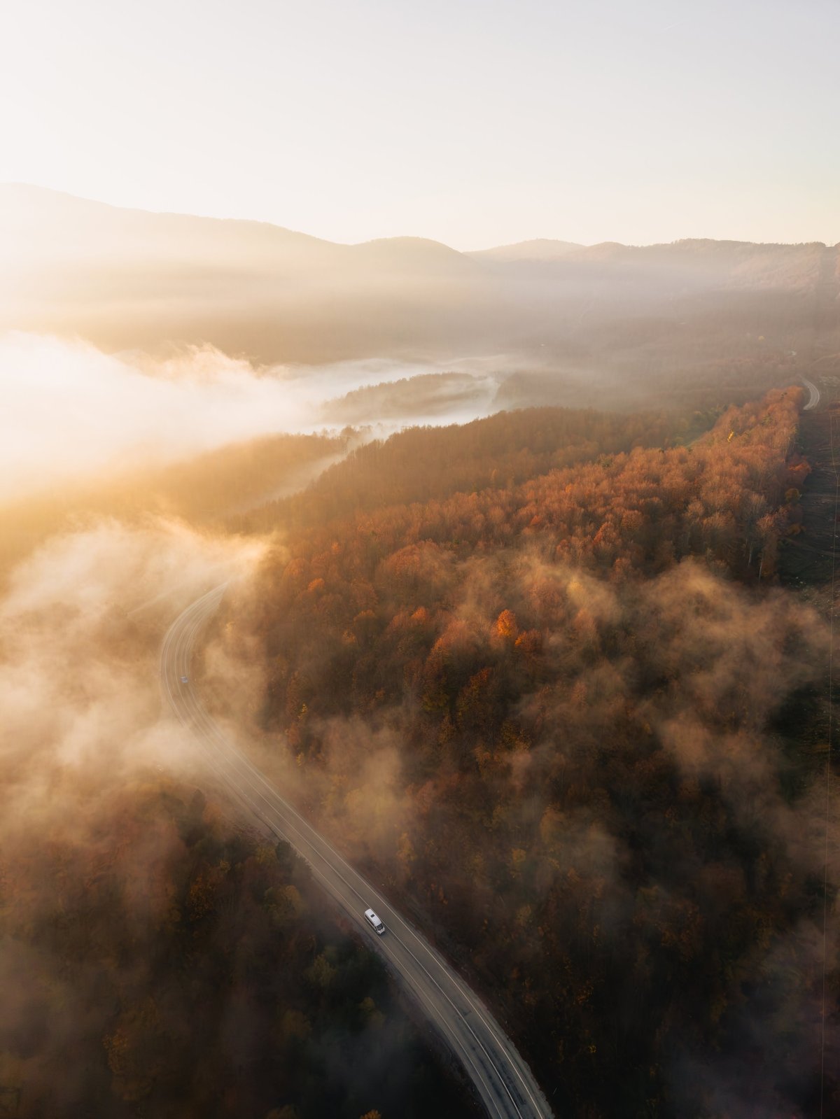 Vista aérea de un vehículo recorriendo una carretera de montaña entre la niebla al amanecer