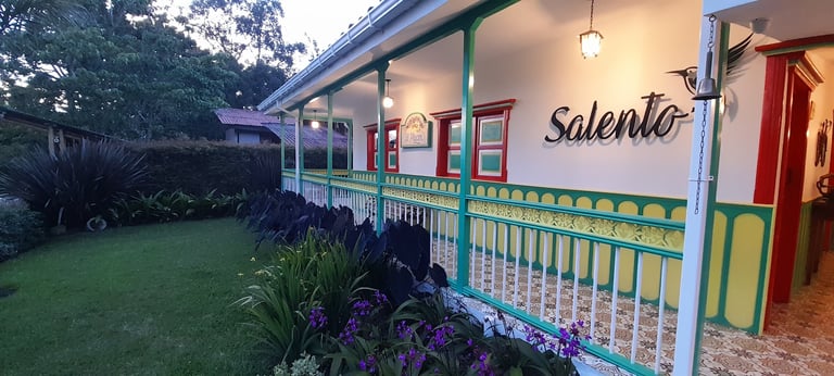 Colorful colonial-style building with green railings, salento sign, and lush garden at dusk